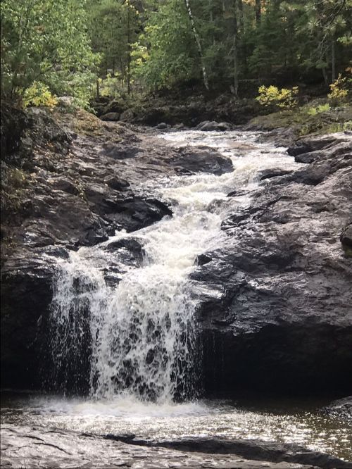 A small waterfall cascades over rocky terrain, surrounded by lush green trees and foliage.