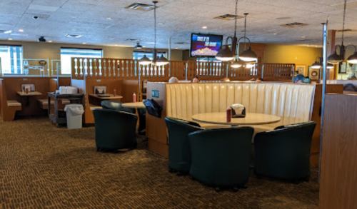 Interior of a restaurant featuring booths, tables, and a TV, with a warm, inviting atmosphere.
