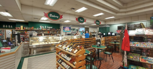 Interior of a grocery store featuring a bakery, deli, and wine section, with shelves and seating areas.