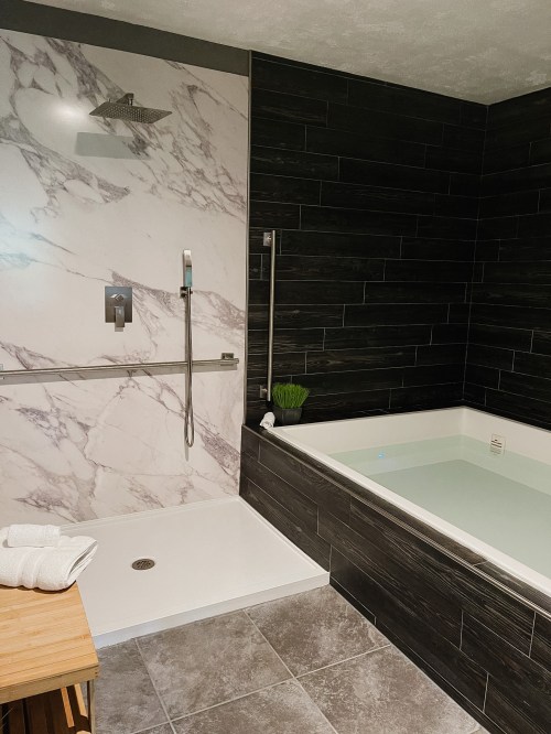 Modern bathroom featuring a sleek shower, a soaking tub, and elegant marble and dark tile accents.