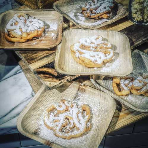A collection of funnel cakes dusted with powdered sugar, served on wooden plates.