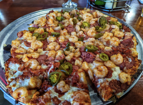 A close-up of a pizza topped with shrimp, jalapeños, and pepperoni on a metal serving tray.