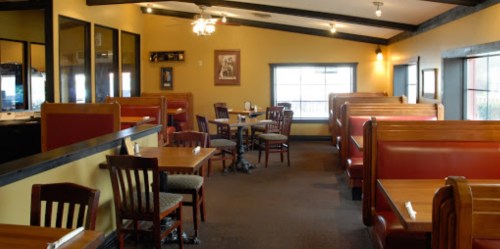 Interior of a cozy restaurant featuring wooden booths and tables, with warm yellow walls and a ceiling fan.