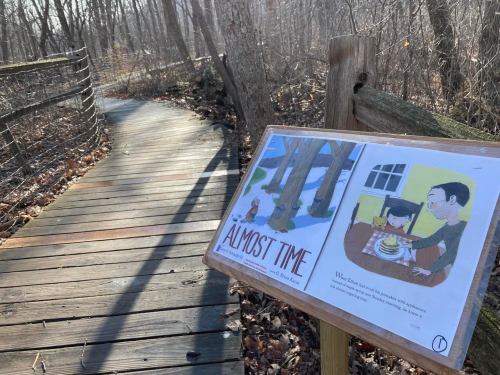 A wooden path through a forest with a sign featuring an illustration and text titled "Almost Time."
