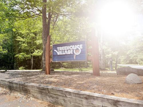 Sign for Treehouse Village surrounded by trees, with sunlight creating a bright effect in the corner.
