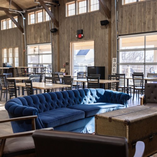 A cozy interior with a blue velvet sofa, wooden walls, and large windows, featuring tables and chairs in a spacious setting.
