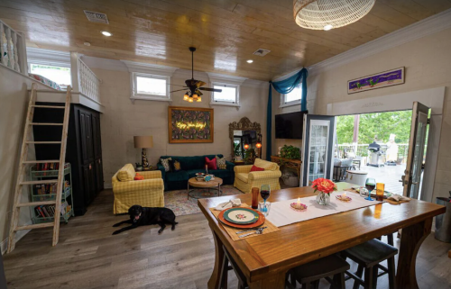 Cozy living room with a dining table, colorful sofas, a dog on the floor, and a view of the outdoor patio.