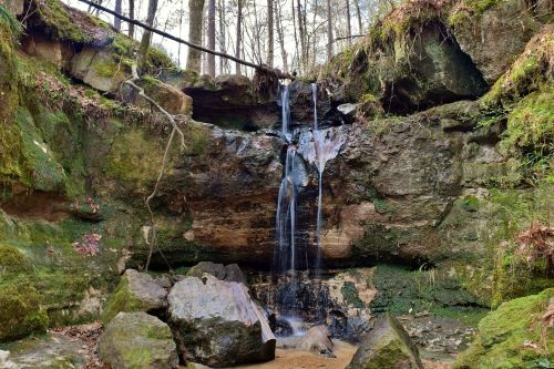 A serene waterfall cascades over moss-covered rocks in a lush forest setting.