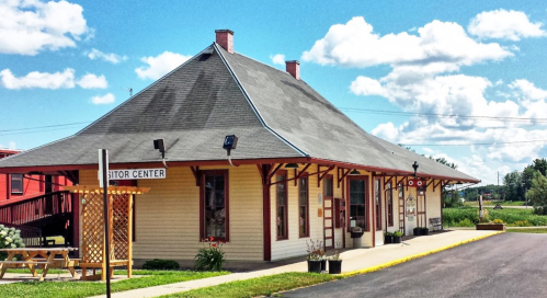 A charming visitor center with a unique roof design, surrounded by greenery and under a blue sky with fluffy clouds.