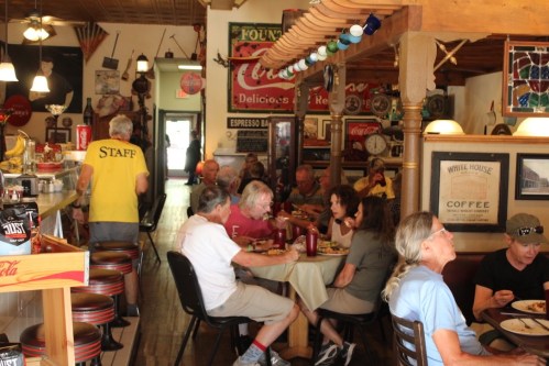 A busy diner with patrons eating at tables and a counter, surrounded by vintage signs and decor.