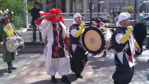 A group of performers in colorful costumes playing drums during a lively street celebration.