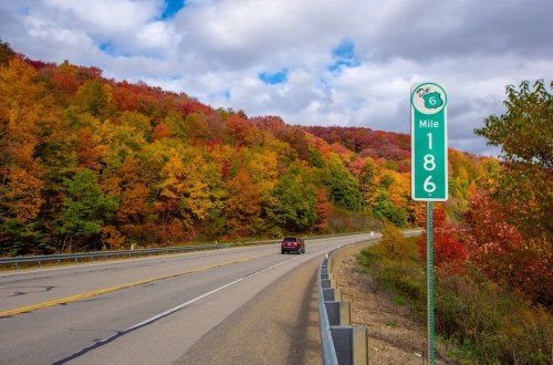 A scenic highway with vibrant autumn foliage on the hills and a mile marker sign indicating Mile 186.
