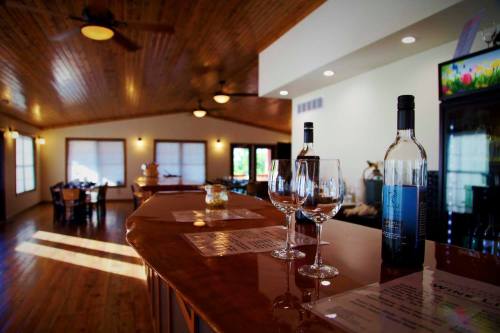 A cozy bar area with wooden accents, featuring wine bottles, glasses, and a dining space in the background.
