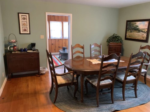 A cozy dining room with a wooden table, eight chairs, and a sideboard, featuring green walls and natural light.
