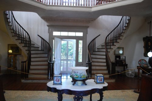 Elegant foyer with a double staircase, a decorative table in the center, and large windows letting in natural light.