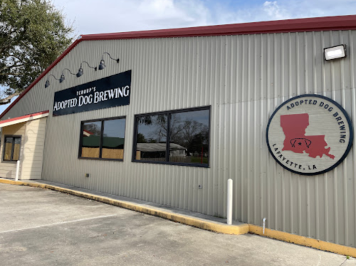 Exterior of Adopted Dog Brewing in Lafayette, LA, featuring a sign and logo on a light-colored building.
