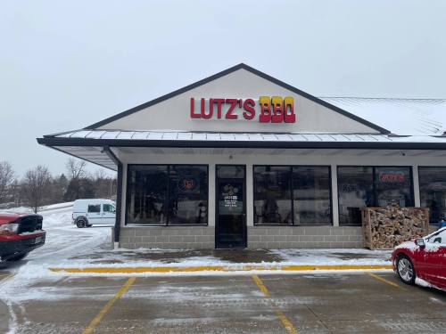 Exterior of Lutz's BBQ restaurant with snow on the ground and parked cars in front.