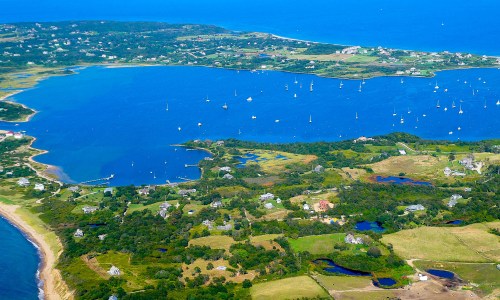 Aerial view of a coastal landscape with blue waters, boats, and lush greenery along the shore.