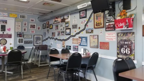 A cozy diner interior with tables, black chairs, and walls decorated with vintage photos and Route 66 memorabilia.
