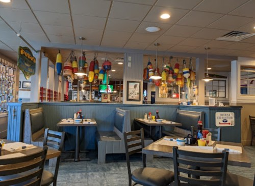 Cozy restaurant interior with booths, nautical decor, and colorful buoys hanging from the ceiling.