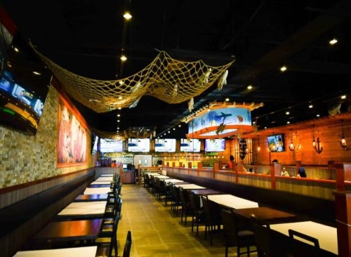 Interior of a restaurant featuring nautical decor, long tables, and multiple screens, with a cozy, inviting atmosphere.