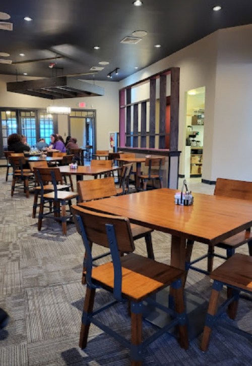 A cozy restaurant interior with wooden tables and chairs, featuring a few diners and warm lighting.