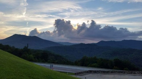 Scenic view of mountains under a cloudy sky at sunset, with lush green hills in the foreground.