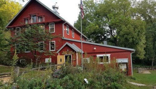 A red wooden building with a flagpole, surrounded by greenery, serving as a nature center.