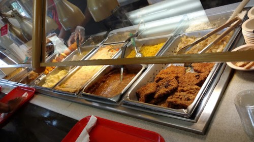 A buffet line with various dishes, including fried chicken, rice, and sides, under warming lamps.