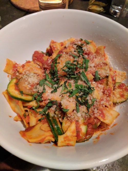 A bowl of pasta with zucchini, marinara sauce, and topped with grated cheese and fresh herbs.