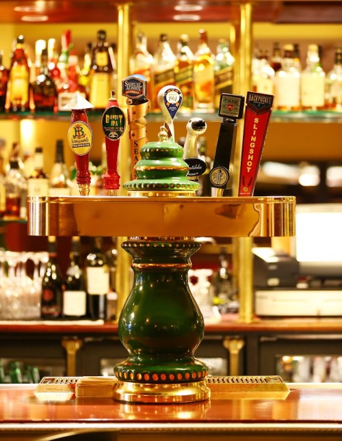 A decorative bar tap with various beer taps, set against a blurred background of bottles on a bar shelf.