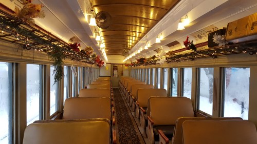 Interior of a vintage train car decorated with holiday garlands and lights, featuring empty rows of seats.