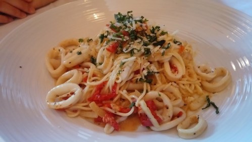 A plate of pasta with calamari, diced tomatoes, herbs, and grated cheese, garnished with fresh parsley.