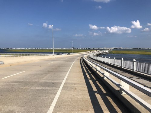 A curved road leads over a bridge with water on both sides and a clear blue sky above.
