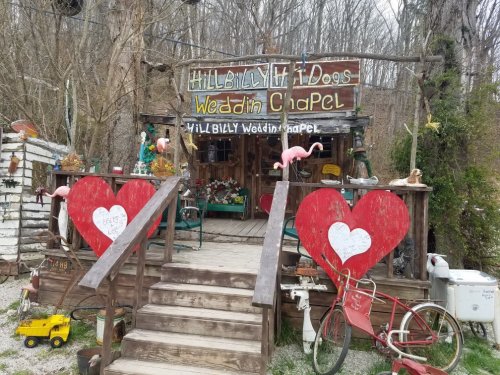 A whimsical wedding chapel with a sign, decorated with hearts and flamingos, surrounded by rustic decor and greenery.