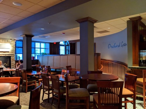 Interior of a cozy restaurant with wooden tables and chairs, featuring a stone fireplace and a softly lit atmosphere.