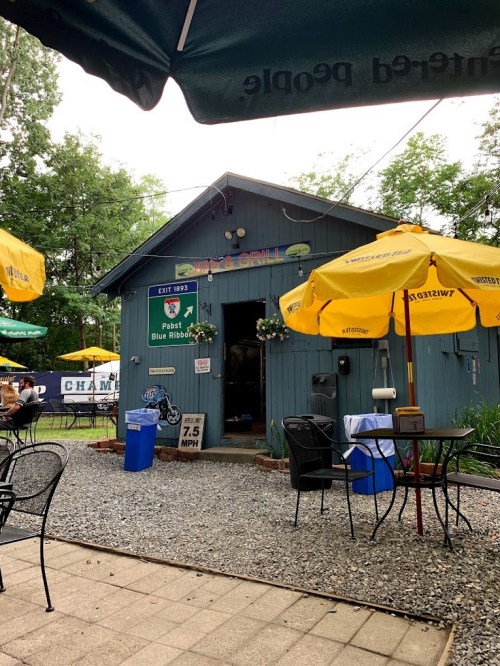 A small blue restaurant with yellow umbrellas outside, surrounded by gravel and greenery.