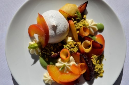 A beautifully arranged dessert featuring meringue, fruits, pistachios, and cream on a white plate.