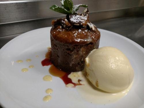 A warm chocolate dessert topped with mint and powdered sugar, served with a scoop of vanilla ice cream on a white plate.