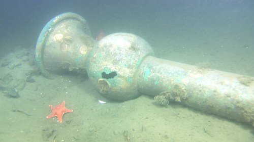 An underwater scene featuring a large, rusty pipe and a starfish on the sandy ocean floor.