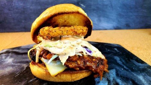 A close-up of a delicious burger with crispy chicken, coleslaw, and a fried onion ring on a toasted bun.