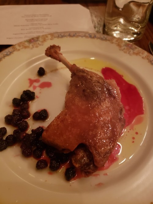 A plate featuring a crispy duck leg with berry sauce and dark berries on the side.