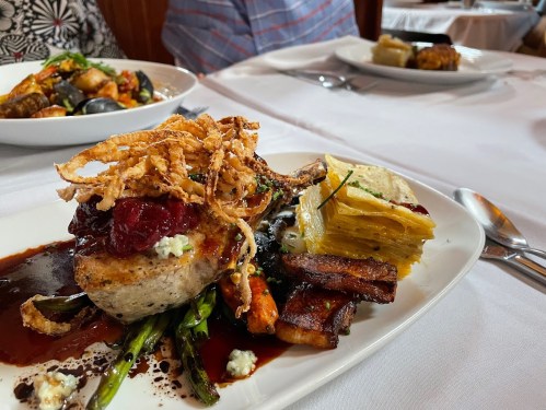 A gourmet dish featuring meat topped with crispy onions, served with asparagus, layered potatoes, and a rich sauce.