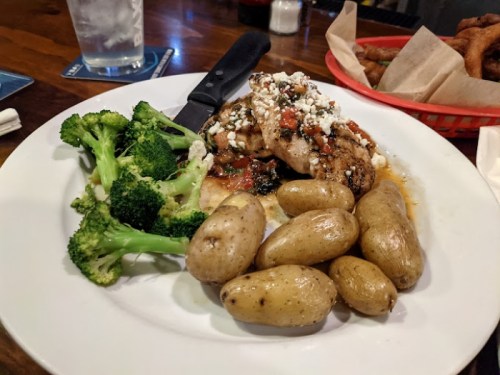 Grilled chicken topped with salsa and feta, served with broccoli and baby potatoes on a white plate.