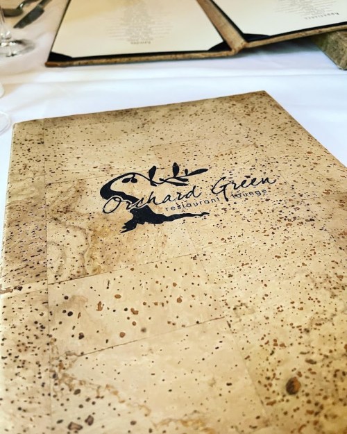 A cork-textured menu cover for Orchard Green restaurant, featuring a simple logo and elegant design.
