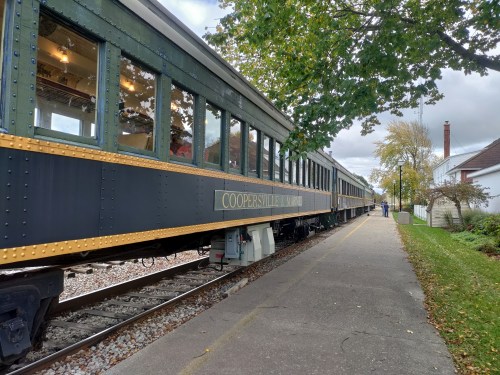 A vintage train car parked beside a sidewalk, surrounded by trees and a residential area.
