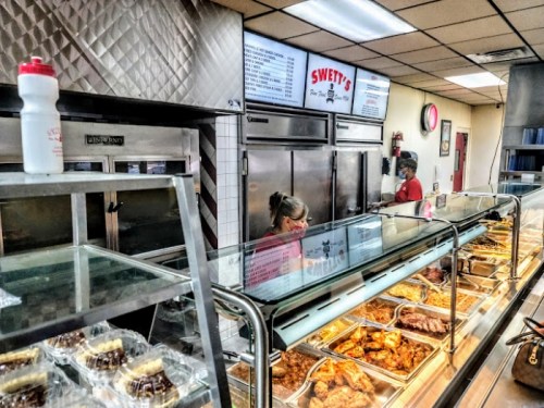 Interior of Swetty's restaurant with a display of food, staff serving, and a menu board in the background.
