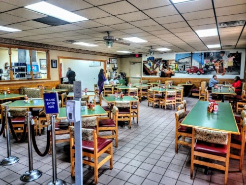 A spacious diner with green tables, wooden chairs, and a mural on the wall, featuring a few patrons and a welcoming entrance.