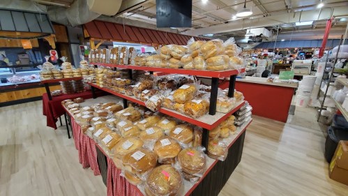 A display of various baked goods on shelves in a market, featuring bread rolls and pastries in clear packaging.