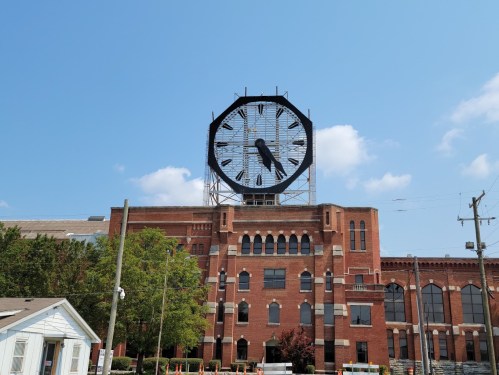 A large clock tower atop a brick building against a blue sky with a few clouds.